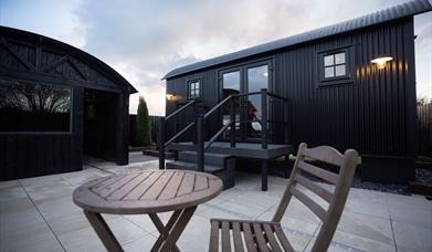 exterior view of the Lodge with outdoor wooden chair and table on paved patio area. 