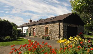 Converted cobblestone barn in the country with red and yellow flowers.