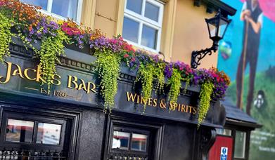 Exterior of Jack's Bar at Walsh's Hotel in Maghera, featuring a black facade with gold lettering that reads "Jack's Bar Wines & Spirits Est. 1760." Co