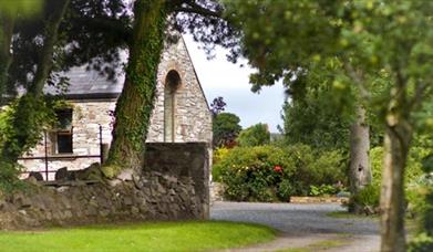 Image shows entrance to property surrounded by trees and bushes.