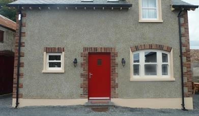 Image shows red front door of stone property with gravel drive