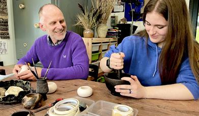 people sat at a table create designs on ceramic pots
