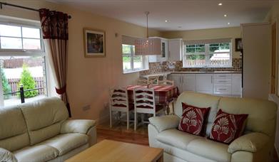 Open plan kitchen, dining and living area with 2 cream 2 seater sofas and dining table with 4 chairs
