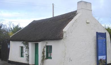 Image of a white cottage with a thatched rood and green door 