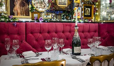 A table with red felt booth seating set with wine glasses and a champagne bottle holding a candle.