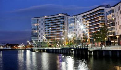 A curving apartment building at night on a seaside walkway.