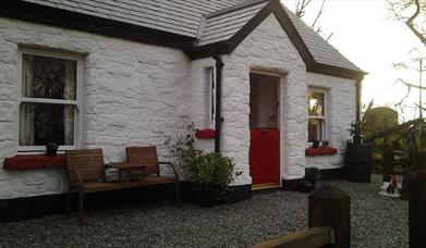 Outside view of cottage with red door and wooden chairs at front