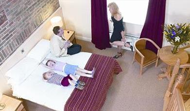 Double bedroom with bed, table and 2 chairs, bedside lockers with lamps.  Image shows family of 4 in room
