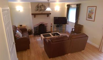 Image shows lounge area with 2 sofas, fireplace and TV