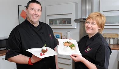 Two teacher chefs smiling and holding plates of food.