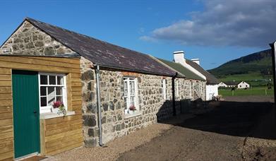 Front exterior view of a stone and wooden cottage connected to other cottages.