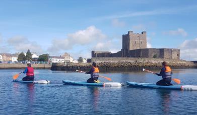 image of 3  paddleboarders kneeling on boards in water in front of Carrickfergus Castle.