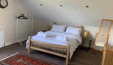 Image shows bedroom in loft with double bed, dressing mirror and clothes rail