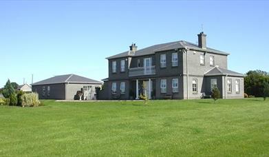 A large BnB on a lawn with a garage and some garden bushes.