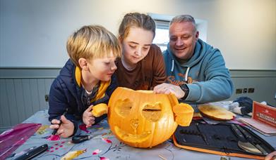 Two children and a man are looking at a pumpkin they have carved together