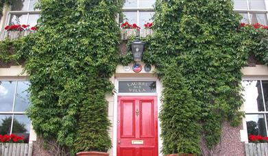 Outside image of Laurel Villa with greenery on walls and red door