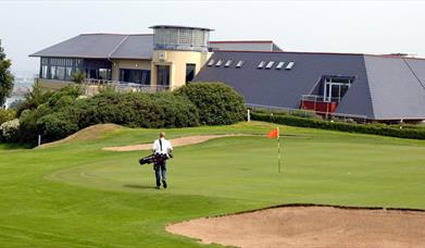 Photo of Club house and a golfer on the green to the forefront
