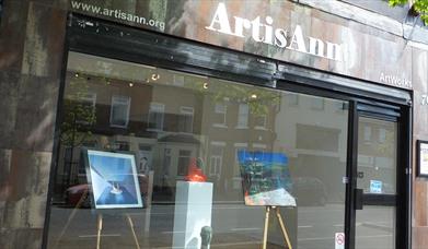 The front exterior of an art gallery with art displayed through a glass front.