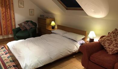 Image shows bedroom with double bed, 2 side tables and 2 chairs. Skylight above the bed.