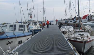 Image shows a walkway and various types of boats in a marina