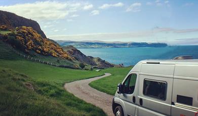 Image shows campervan on road leading down to the sea