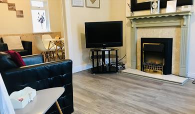 A living room with a fireplace, chair and TV leading to a dining area.