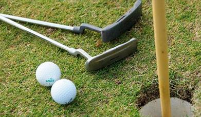 Close up photo of two putting sticks and two golf balls beside putting hole and flag at Seapark