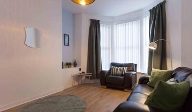 A living room with a leather sofa, armchair, and a bay window with blinds and curtains.