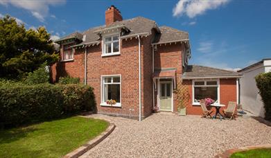 exterior of a semidetached cottage with a stone driveway, a lawn and some garden furniture.