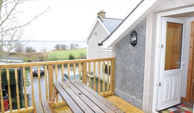 A decked entrance to a second story loft cottage with a picnic table and a view of a lake.