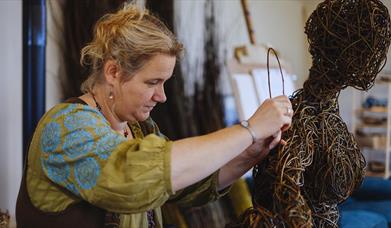 A lady at work on a weaving sculpture resembling a person