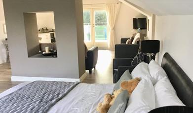 Image shows double bed with teddy bears and sitting area with patio doors to outside