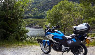Image shows motorcycle parked at scenic area with view of river between trees