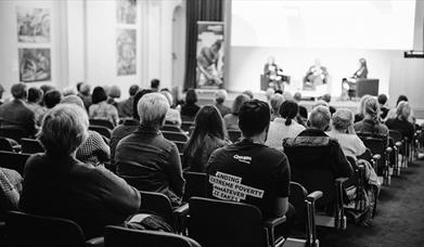 audience watching a discussion panel of 3 people on stage 