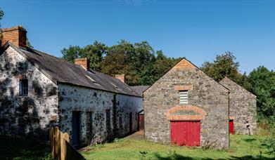 Stone buildings with red doors in a grassy area under a clear sky.
