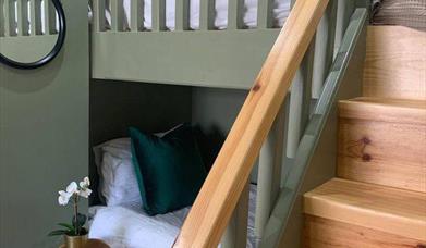 Image is of loft bedroom with bunk beds with wooden stairs up to top bunk