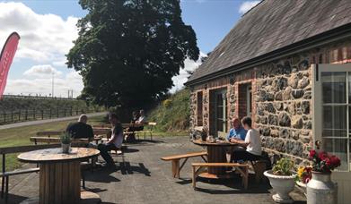 Stone cottage with people dining outside at picnic tables.