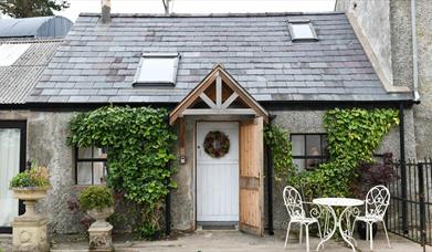 Outside view of Milk House with greenery on the walls and outside table and 2 chairs