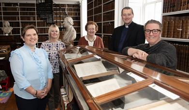 Five people standing around a glass topped display cabinet containing books.