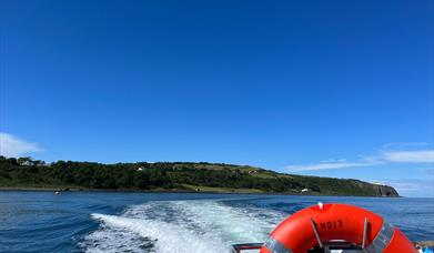 View of Blackhead path and Lighthouse with wake of sea behind boat and life ring visible on Charter NI Boat