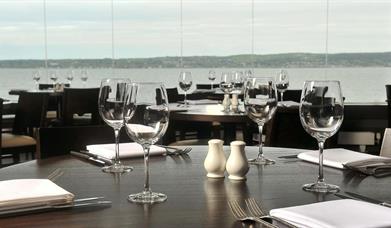 Waterfront restaurant with many tables set with wine glasses, cutlery and salt and pepper shakers.