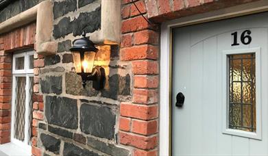 Image shows front door of No 16 with lantern on the brick wall outside