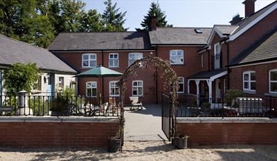 Image shows front of property with archway entrance and small courtyard with seating area