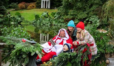 Three children are laughing and sitting with Santa in his sleigh on the grounds of Hillsborough Castle and Gardens. Santa is in a red suit.