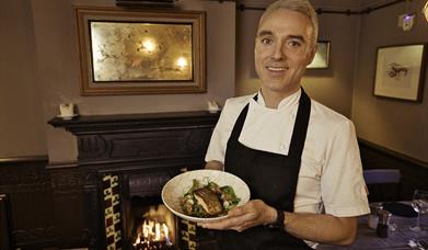 Chef holding a plate of food in front of an open fire