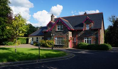 Rossclare Lodge front view of the house. A large lawn area in front of a large house in Donegal stone and a smaller painted extension to the left. A d