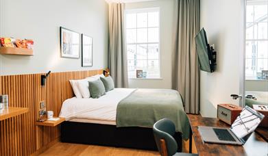 Image shows a double bed in a hotel room with paintings of Northern Ireland on the background wall