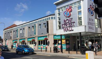 Image shows entrance to Bow Street Mall with visitors exiting the mall and cars driving by