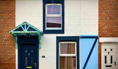 A painted terrace house designed with a light blue window shutter and canopy.