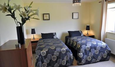 Twin bedroom with 2 single beds with bedside lockers and bunch of flowers in image